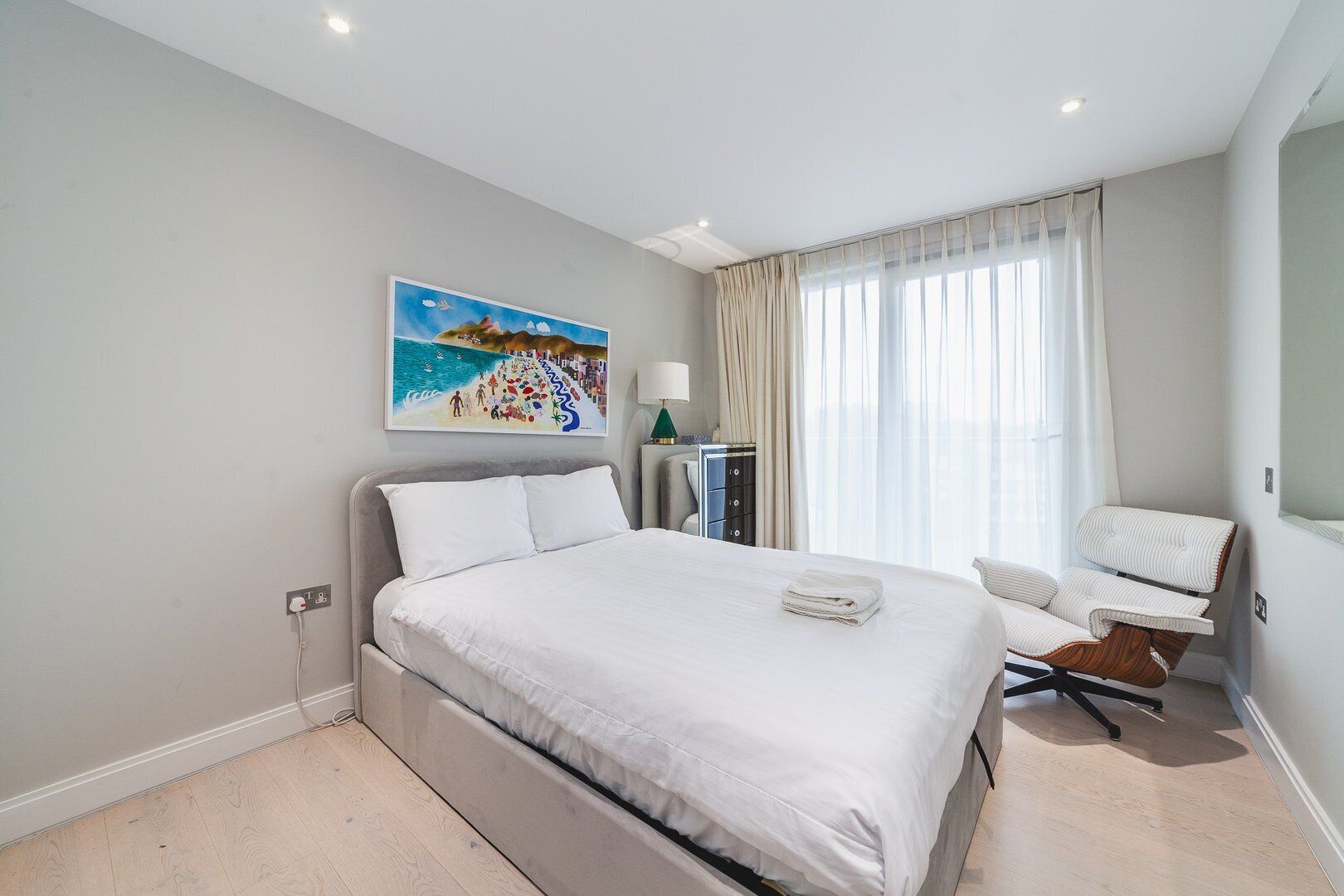Een moderne hotelkamer met een groot bed, een bureau en een stoel. Er hangt een schilderij aan de muur en er is een raam met gordijnen.