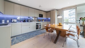A modern kitchen with a central island, built-in appliances, and a dining area with a large window. - Stylish Three-Bedroom Battersea Flat (London)