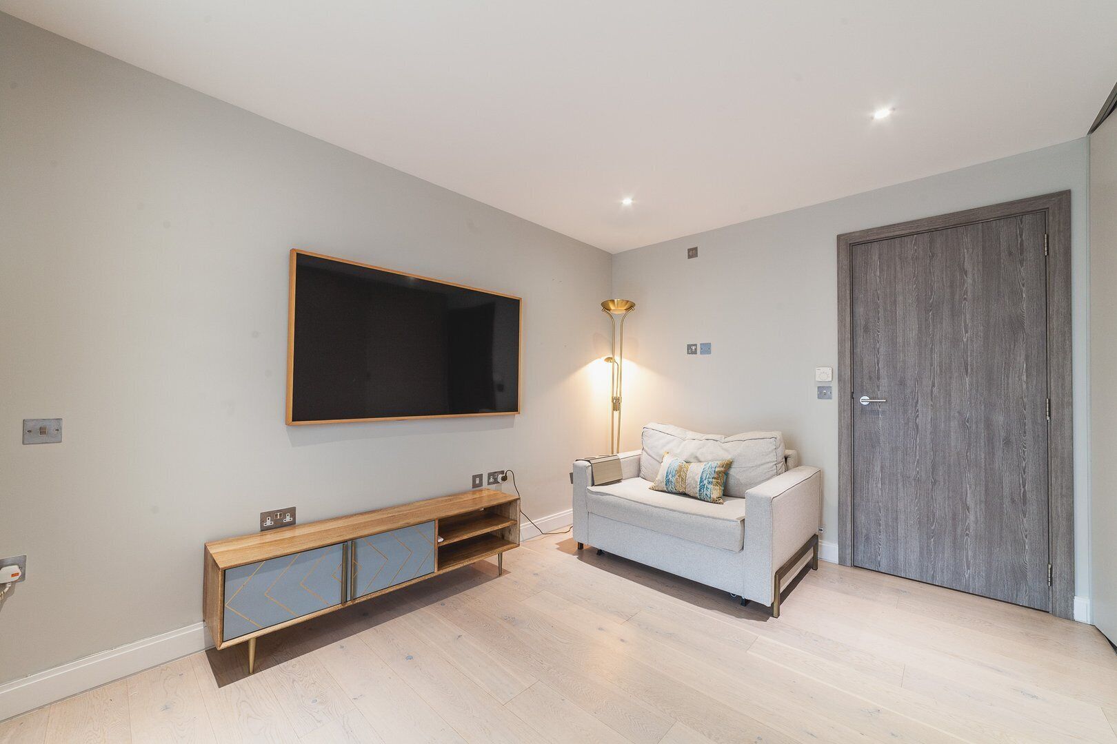 A modern living room with a flat-screen TV, a sofa, a floor lamp, and a wooden cabinet.