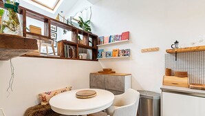 A compact kitchen with a round table, two chairs, a small cabinet, and a trash bin.