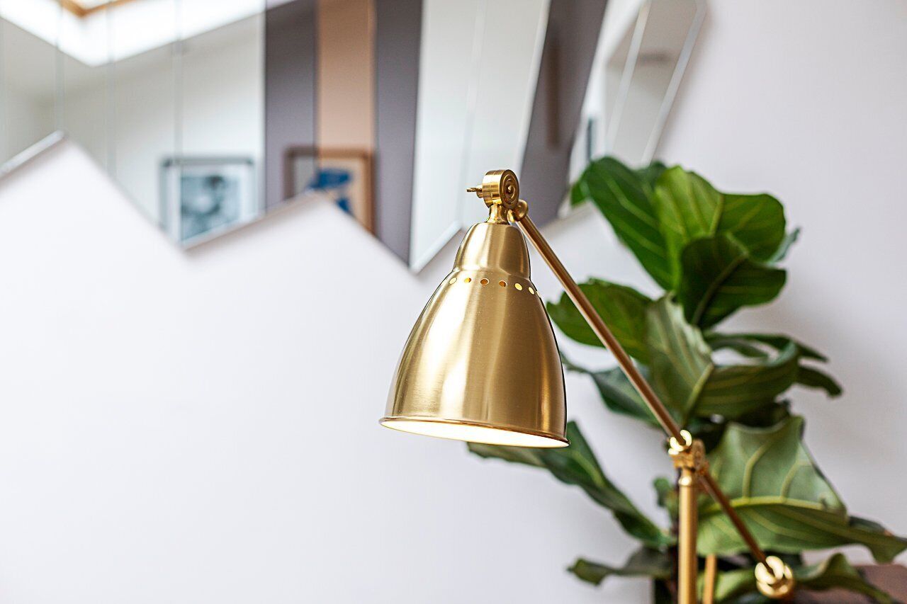 Een gouden bureaulamp met een reflecterend oppervlak, voor een grote groene plant geplaatst.
