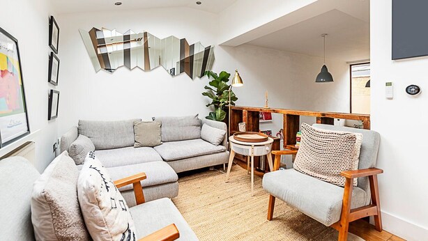 A modern living room with a grey sofa, a wooden chair, a round table, and a large mirror on the wall.
