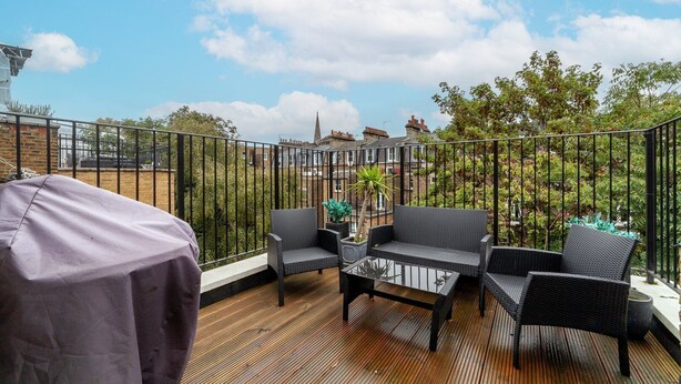 A balcony with a wooden deck, black metal railing, and two wicker chairs with a small table.