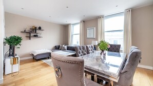 A modern living room with a large L-shaped sofa, a dining table with chairs, a small side table, and a potted plant.