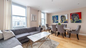A modern living room with a grey sofa, a marble coffee table, and a dining area with grey chairs and a wooden table.