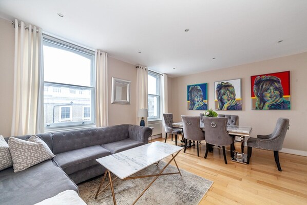 A modern living room with a grey sofa, a marble coffee table, and a dining area with grey chairs and a wooden table.