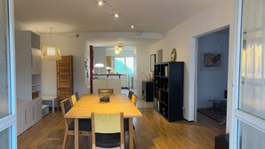 Un comedor amplio con una mesa y sillas de madera, una cocina al fondo y una estantería.