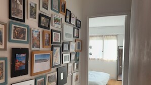 Un pasillo con una pared llena de cuadros, que conduce a un dormitorio con una cama y un ventanal.