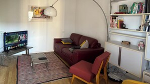 Una sala de estar con un sofá rojo, una mesa de centro, un televisor, una estantería y un cuadro en la pared.