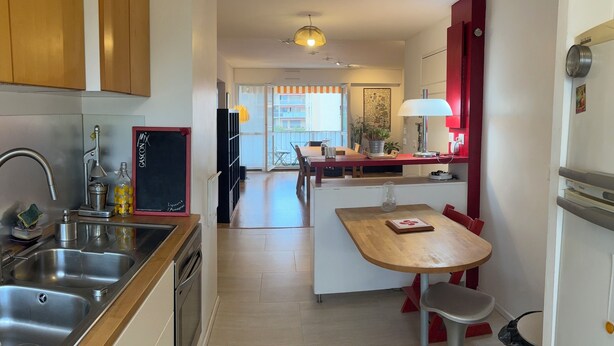 Una cocina moderna con electrodomésticos de acero inoxidable, encimera de madera y comedor con una silla roja y una mesa.