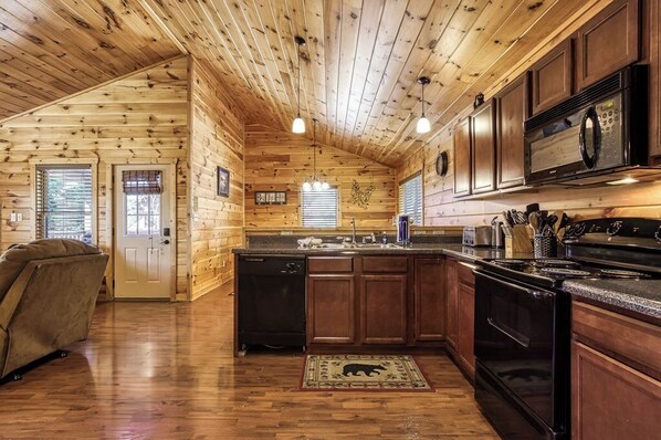 A log cabin interior with a kitchen featuring wooden cabinets, a black stove, and a microwave. - Starwood, Hot Tub, Mtn Views, $560 In tickets each paid day (Pigeon Forge)