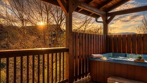 Eine Holzterrasse mit Whirlpool, einer Sitzbank und Blick auf Bäume und Berge.