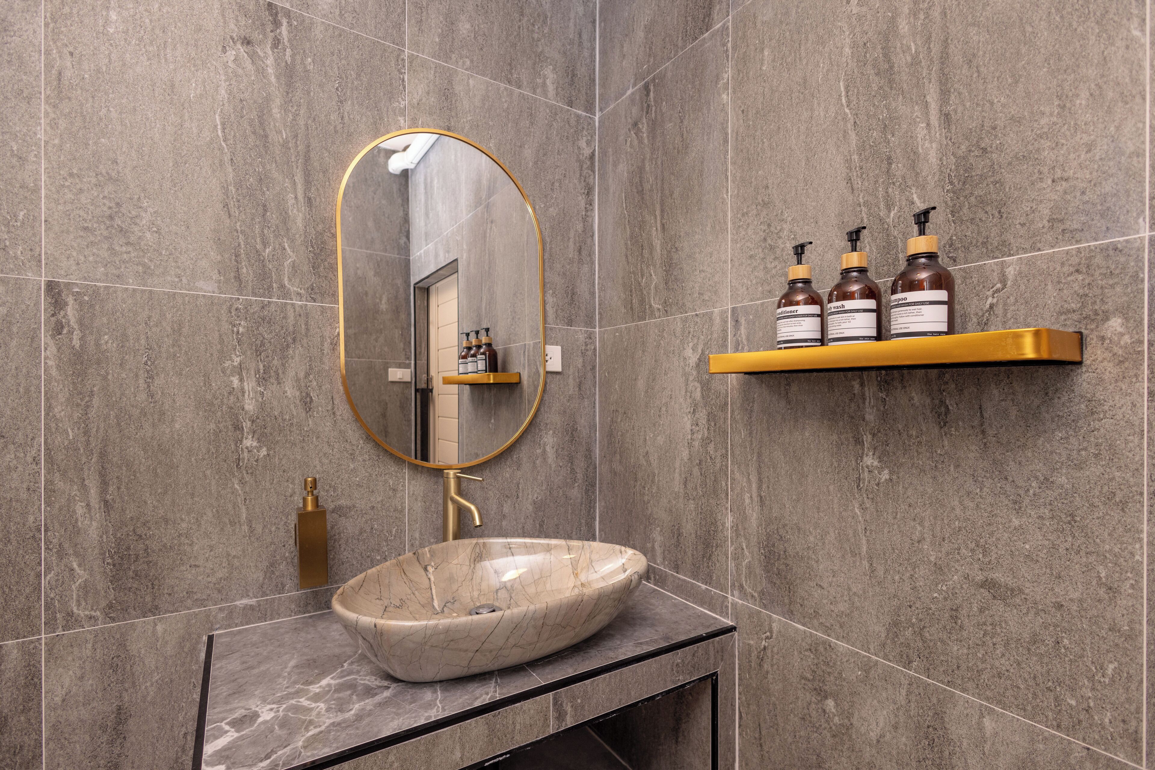 A bathroom with a marble sink, a gold-framed mirror, and a shelf with toiletries.