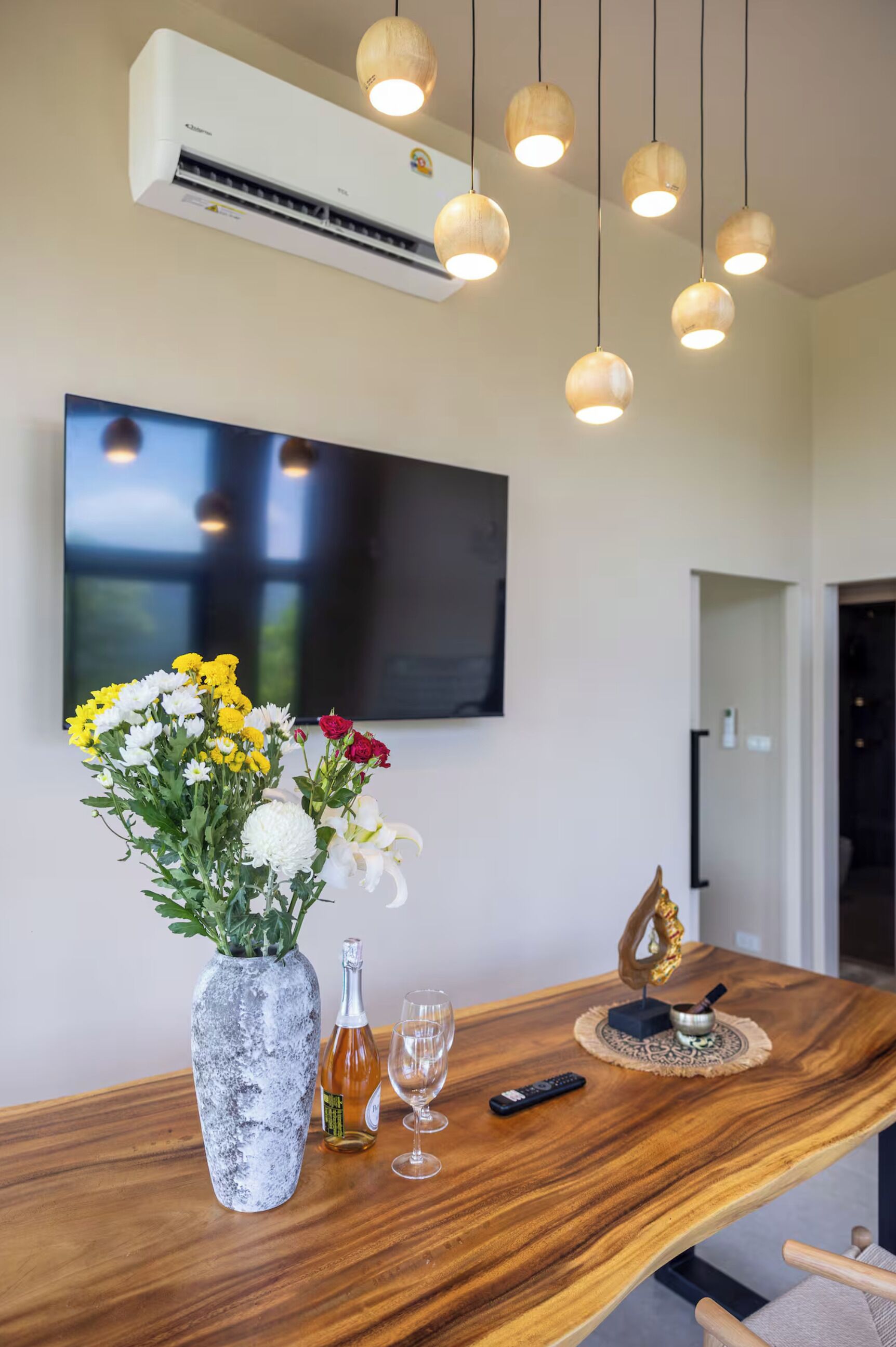 A dining area with a wooden table, a vase of flowers, a bottle, and a remote control.