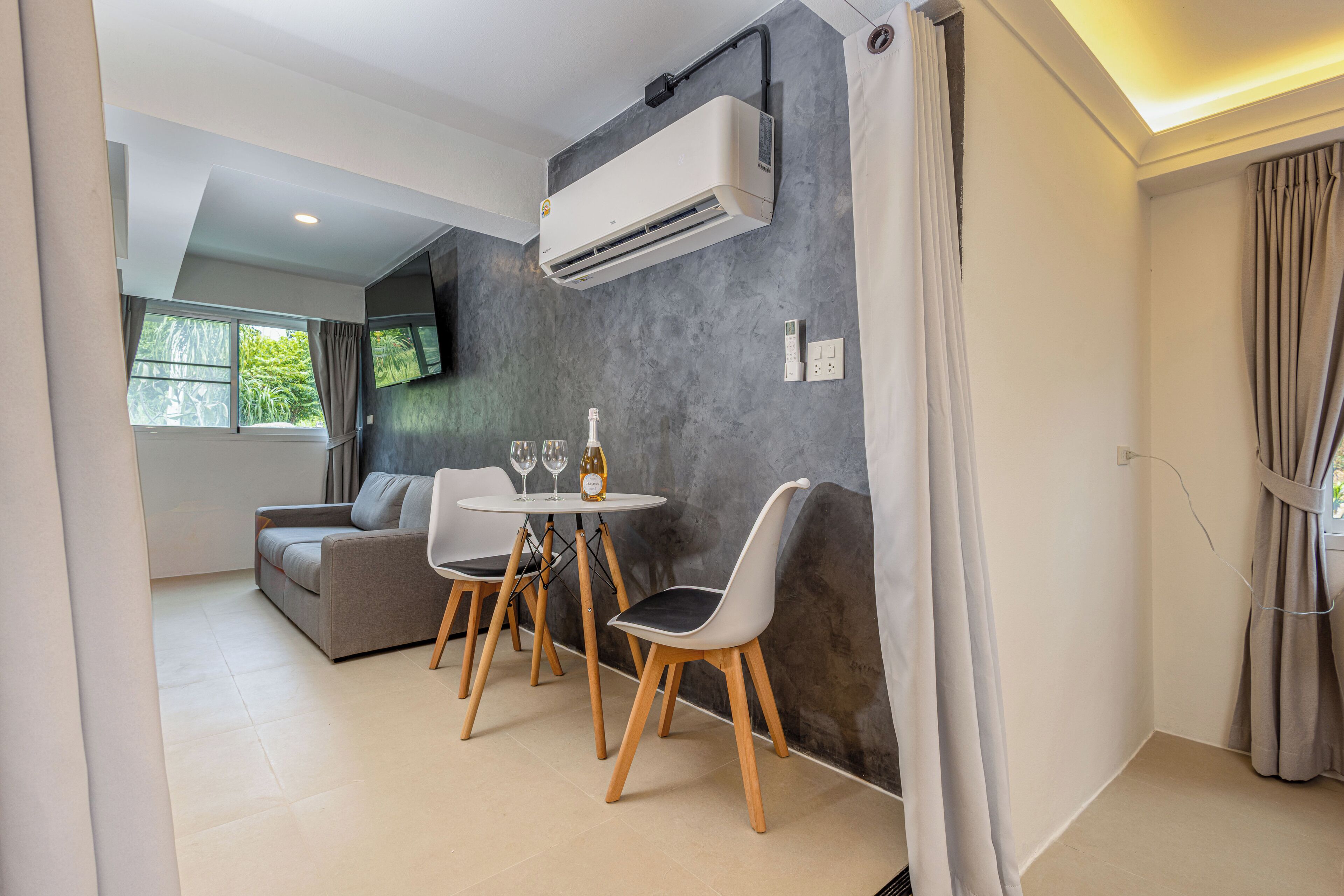 A modern living room with a gray sofa, a round table with chairs, and an air conditioning unit mounted on the wall.
