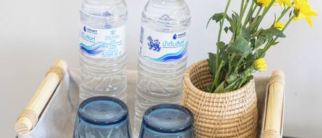 Una bandeja de mimbre con dos botellas de agua, un florero con flores amarillas y dos recipientes de vidrio sobre una superficie oscura.