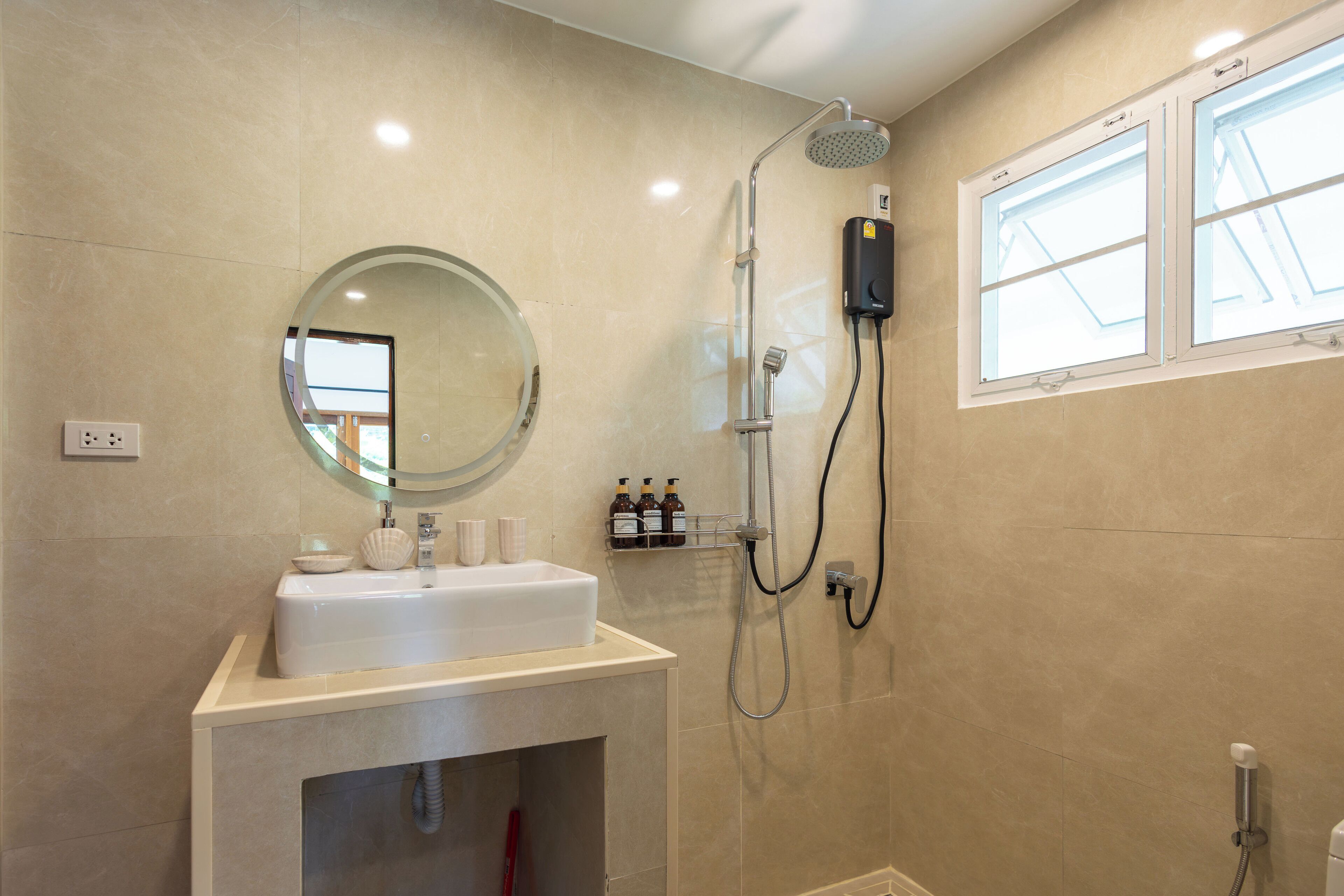 A bathroom with a sink, mirror, shower, and window.
