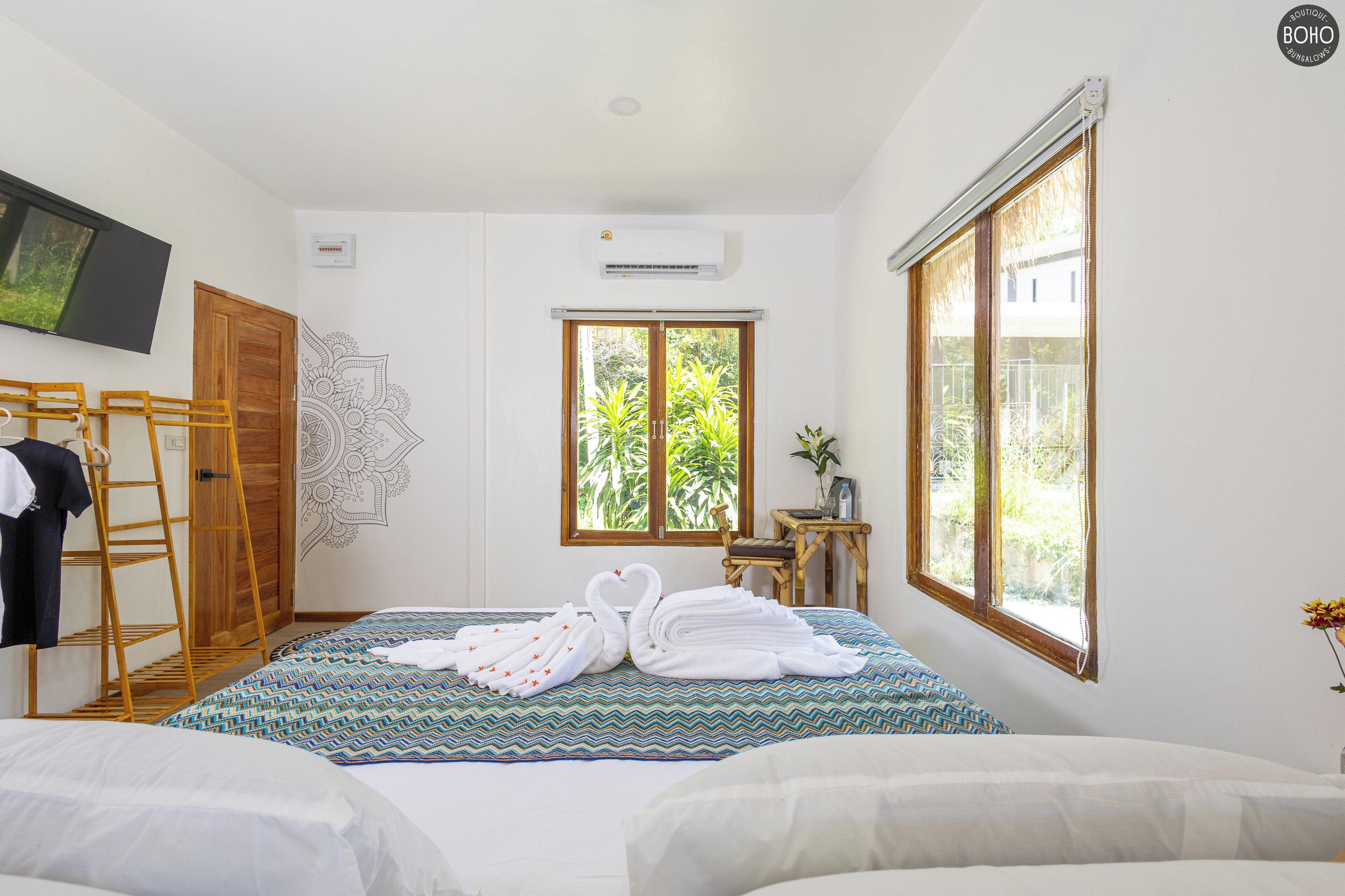 Une chambre d’hôtel comprenant un lit, une échelle en bois, un téléviseur fixé au mur, un climatiseur, une fenêtre donnant sur un paysage verdoyant et un élément décoratif mural.