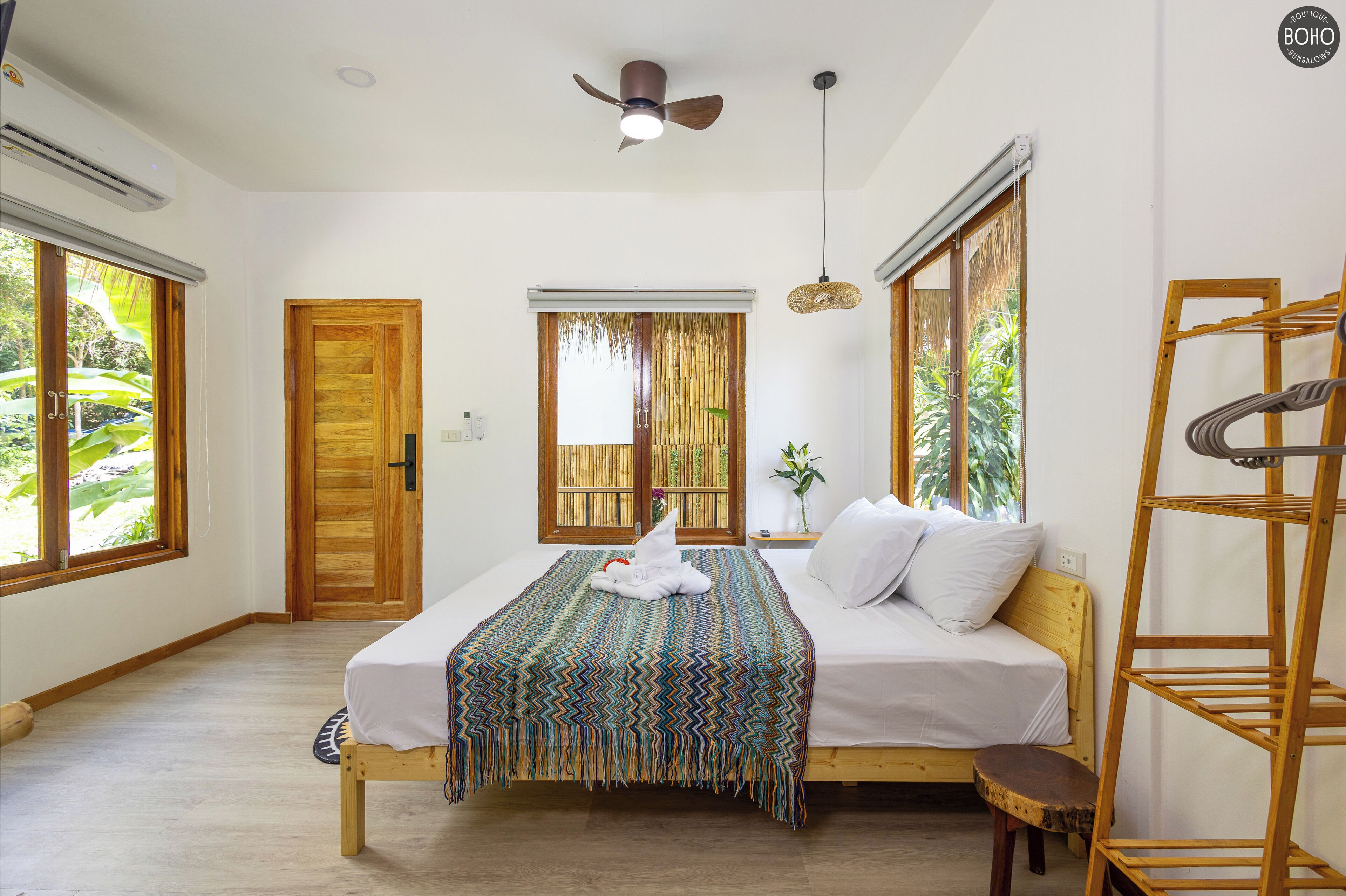 A bedroom with a bed, wooden door, windows, ceiling fan, and a wooden shelf.