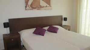 Una cama bien hecha con dos almohadas, un cabecero de madera, dos mesitas de noche con lámparas y un cuadro colgado en la pared.