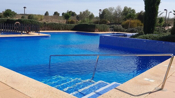 Una piscina con agua azul cristalina, rodeada por un suelo de baldosas y una valla de madera.