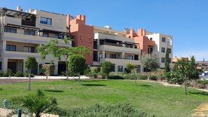 Un edificio residencial de varios pisos con balcones, césped verde y una zona de estacionamiento.