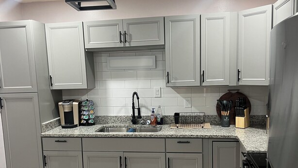 A modern kitchen with grey cabinets, a granite countertop, a built-in oven, and a coffee maker.