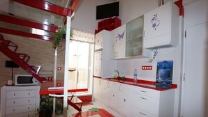 Una cucina compatta con mobili bianchi, un piano di lavoro rosso e un forno a microonde.