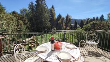 A round outdoor table with metal chairs, a bottle, and plates on a balcony with a metal railing.