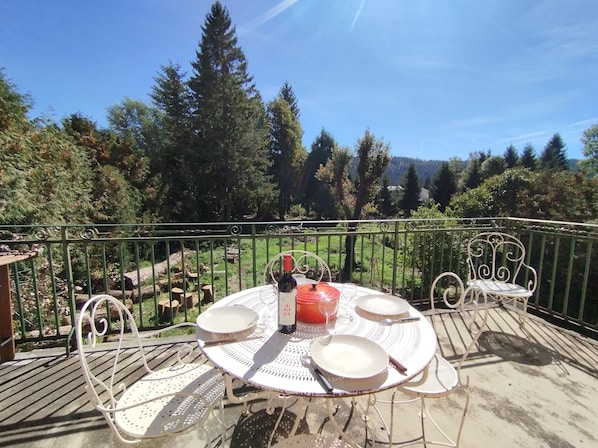 A round outdoor table with metal chairs, a bottle, and plates on a balcony with a metal railing. - Jura-style house with a garden in the heart of the village of Mouthe (Mouthe)