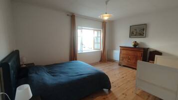 A bedroom with a bed, a nightstand, a dresser, a window with curtains, and a ceiling fan.