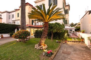 A courtyard with a palm tree, a flower bed, and a pathway leading to a building with balconies.