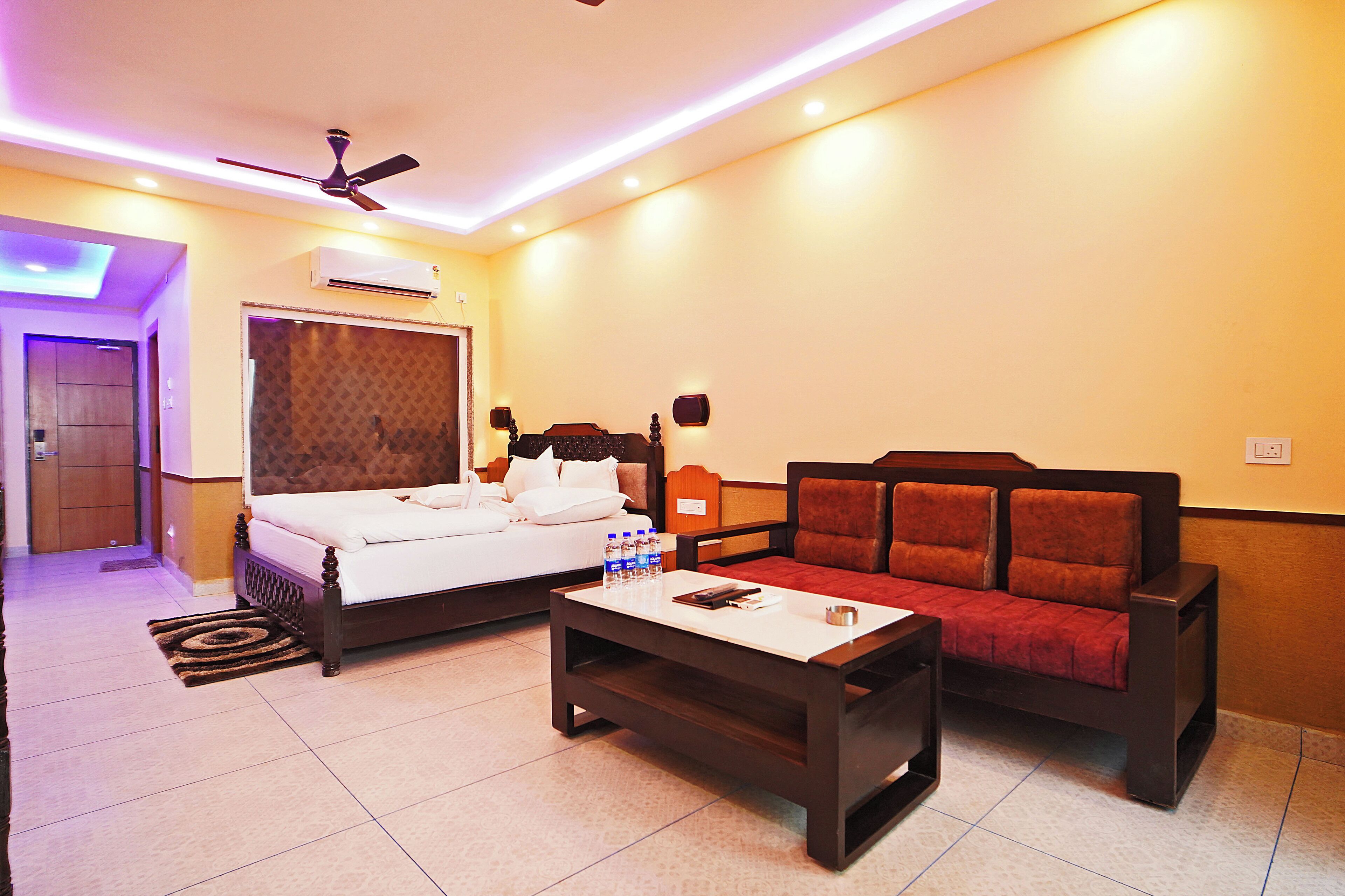 Habitación de hotel con cama, sofá, mesa de centro, ventilador de techo y aire acondicionado.
