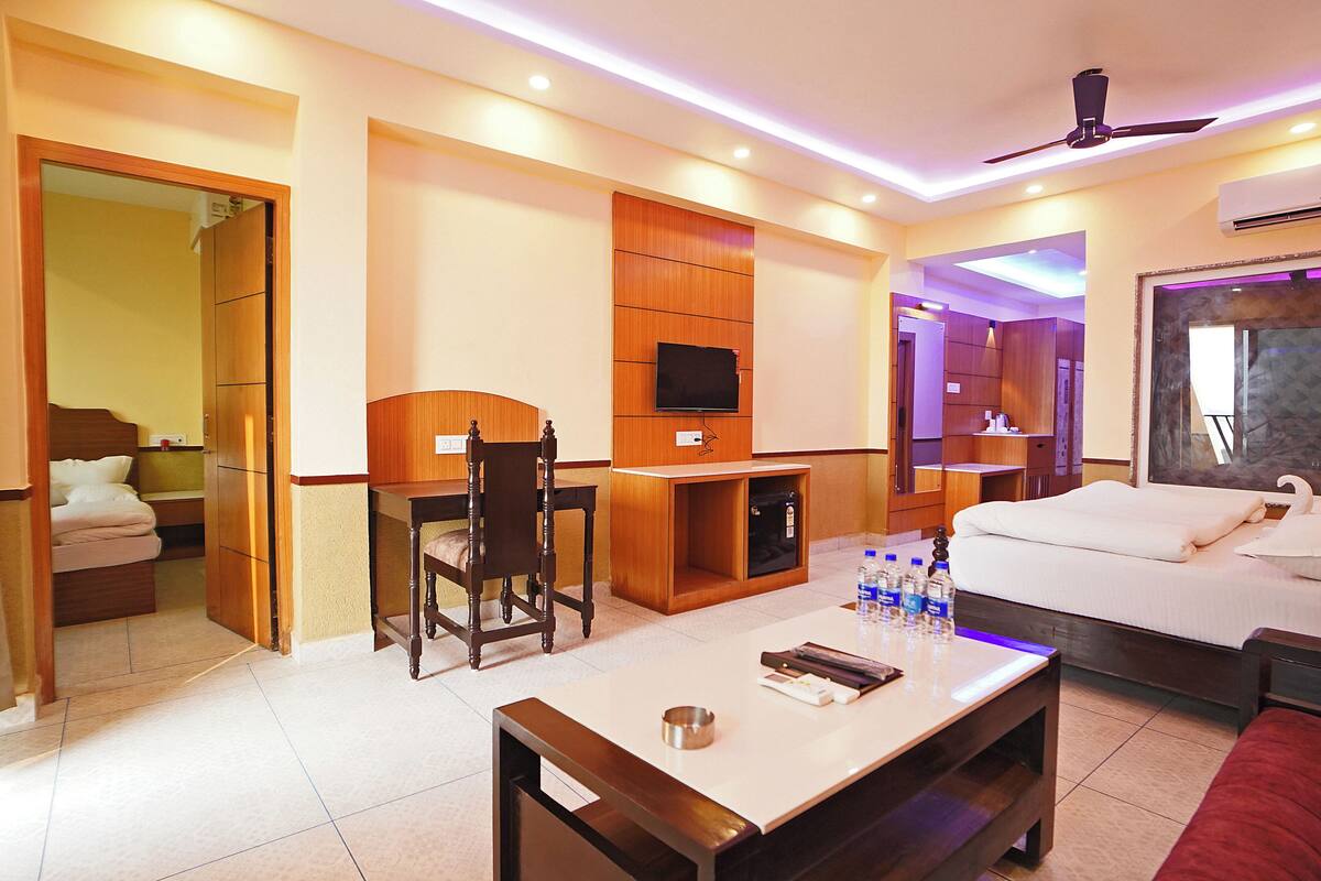 A hotel room with a bed, a desk with a chair, a TV, and a minibar.