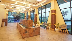 Eine großzügige Lobby mit Empfangstresen, Sitzgelegenheiten, großen Fenstern und Deckenventilatoren.