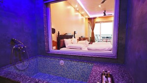 Ein modernes Badezimmer mit einer großen Badewanne, einer Duschkabine und einem Fenster mit Blick ins Zimmer.