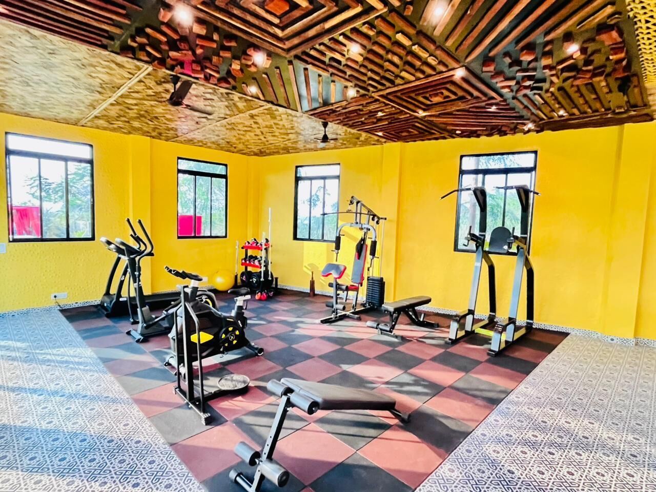 Une salle de sport équipée de matériel d’exercice, dotée de grandes fenêtres et d’un sol à motifs.