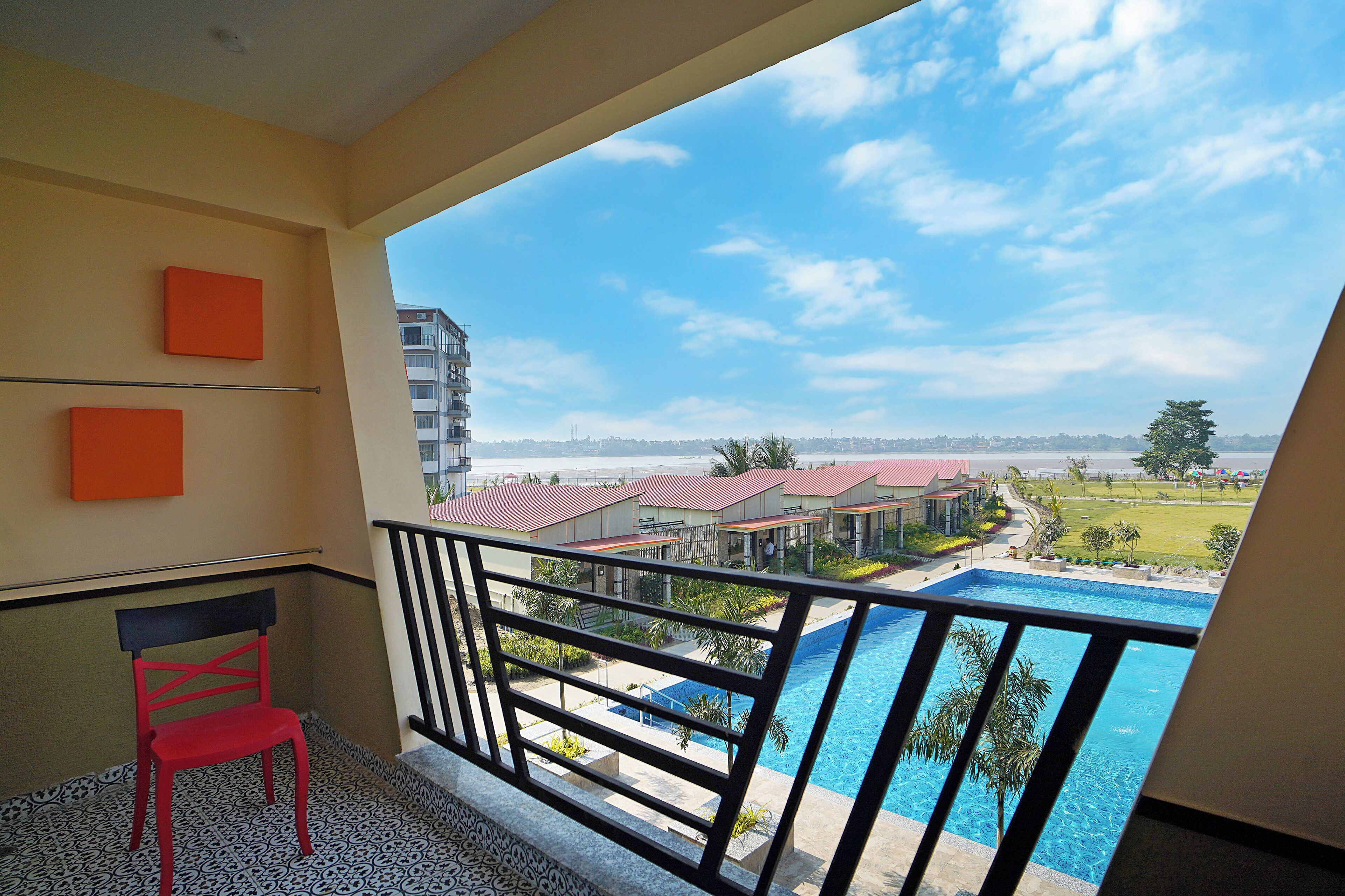 A balcony with a red chair, a pool, and a view of buildings and greenery.
