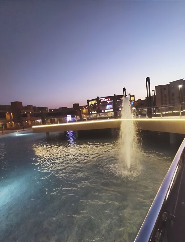 Vista nocturna de una fuente de agua con un puente al fondo.