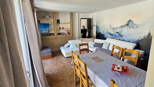 Una habitación acogedora con una mesa de comedor, sillas de madera, un sofá y un mural con un paisaje de montaña.