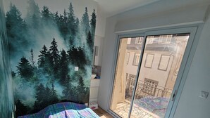 Un dormitorio con cama, un mural de un bosque, una puerta corredera de vidrio y vistas al balcón exterior.