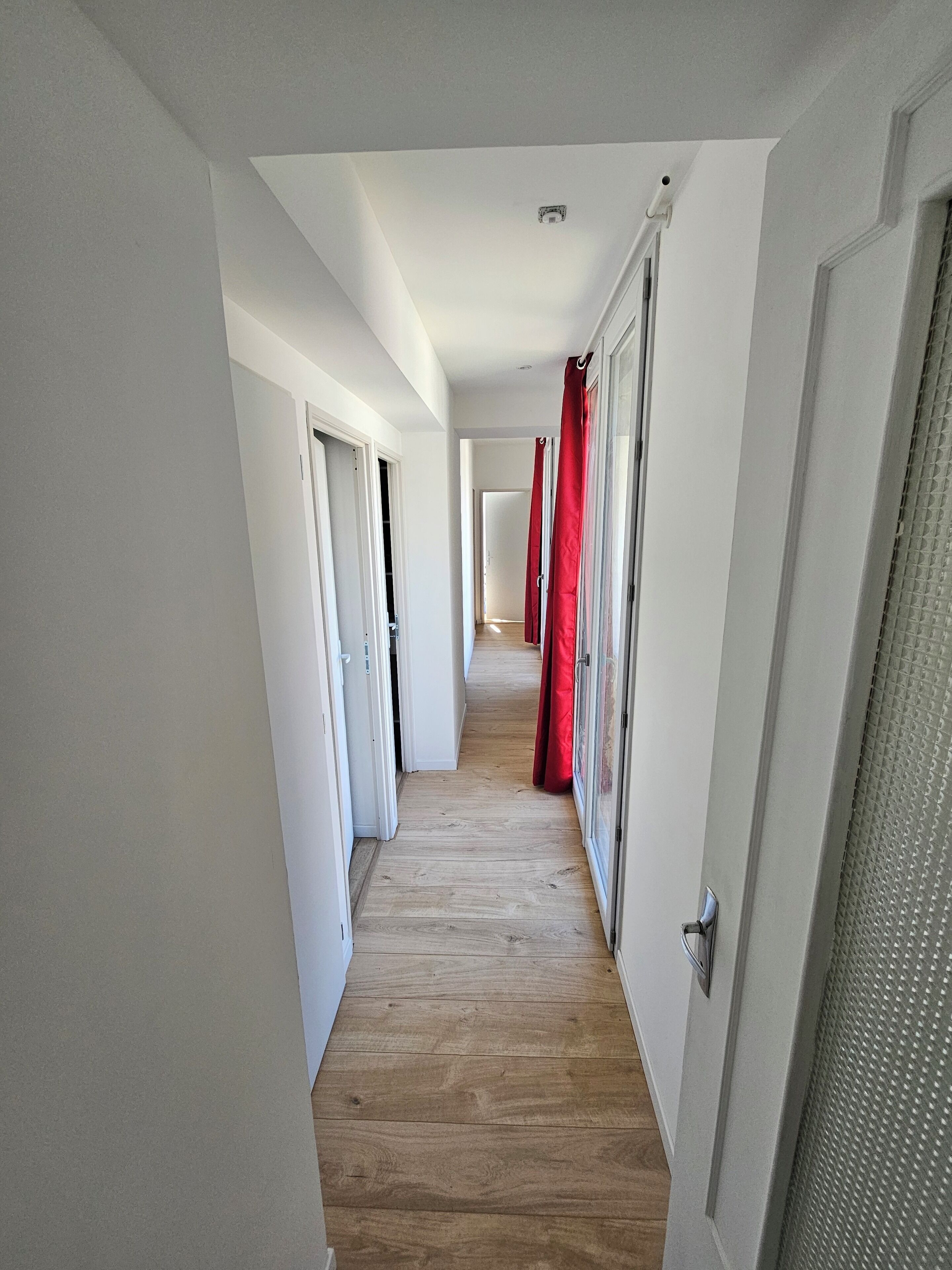 Um corredor com piso de madeira, paredes brancas e portas que dão para os quartos.