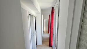 Un pasillo con suelo de madera, paredes blancas y puertas que dan a habitaciones.