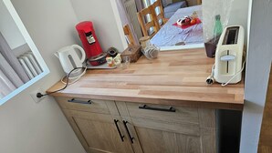 Una pequeña kitchenette con una encimera de madera, un dispensador de agua rojo, una cafetera, un tostador y un bol de fruta.