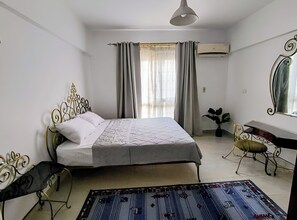 A bedroom with a bed, a desk, a chair, a potted plant, and a mirror.