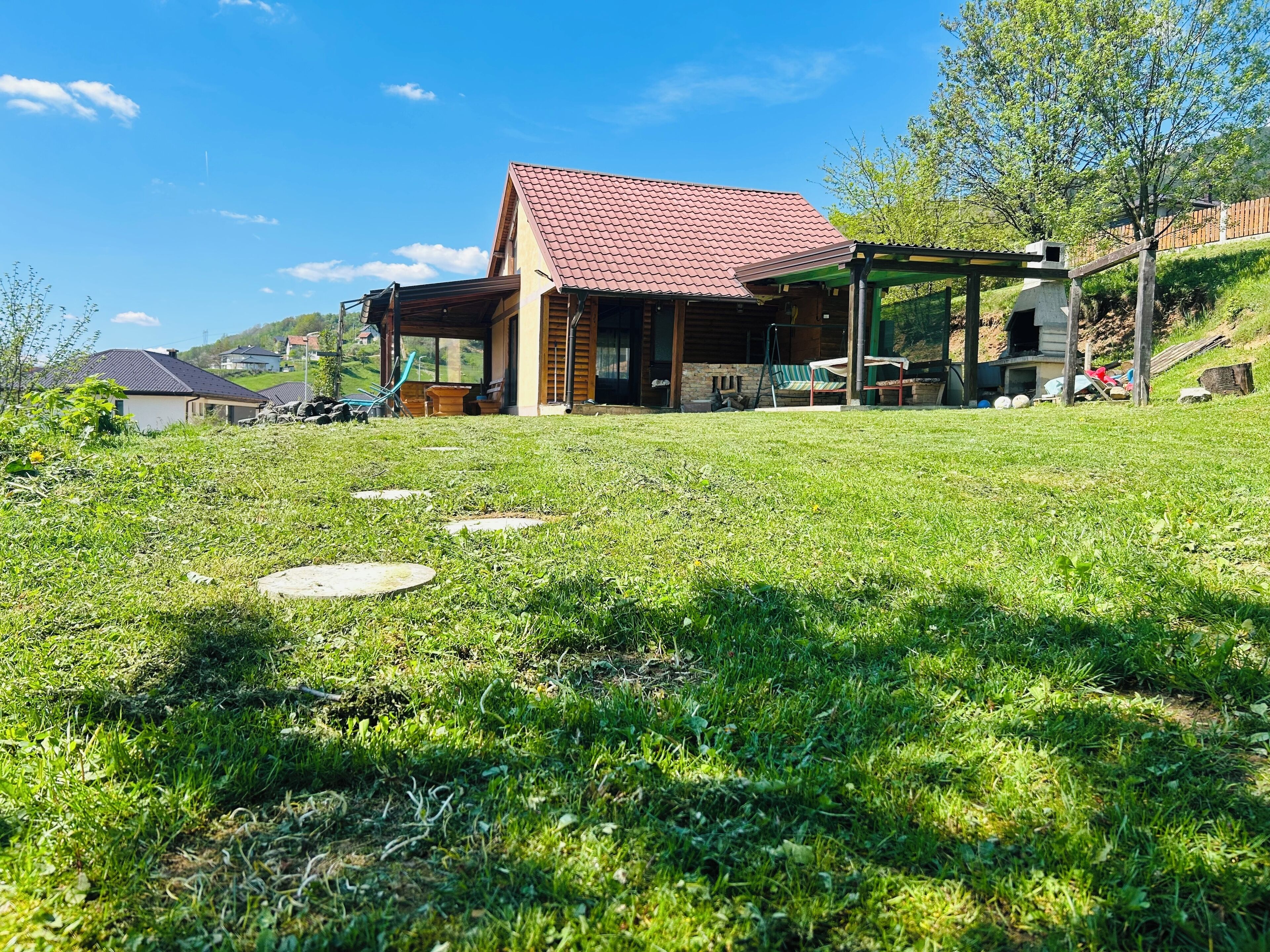 A house with a red-tiled roof, a covered porch, and a grassy yard with stepping stones.