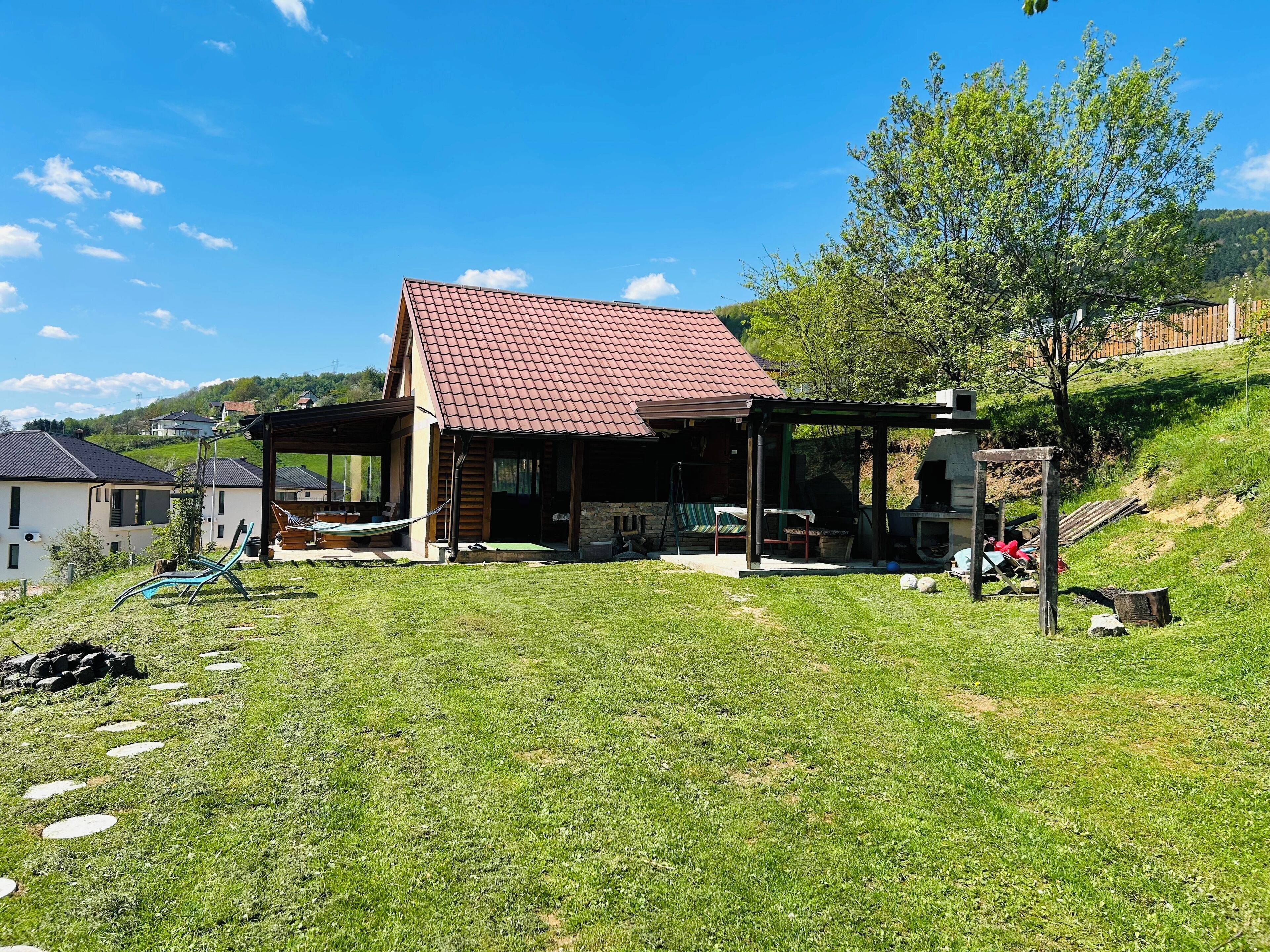 Ein Haus mit rotem Ziegeldach, einer überdachten Terrasse und einem Rasen mit trittfesten Steinen.