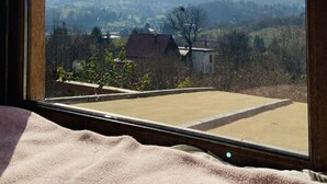 Una habitación con un ventanal grande que da a un paisaje rural con montañas y casas dispersas.