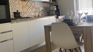 Een moderne keuken met witte kastjes, een betegelde achterwand, een gasfornuis en een eethoek met een tafel en stoelen.