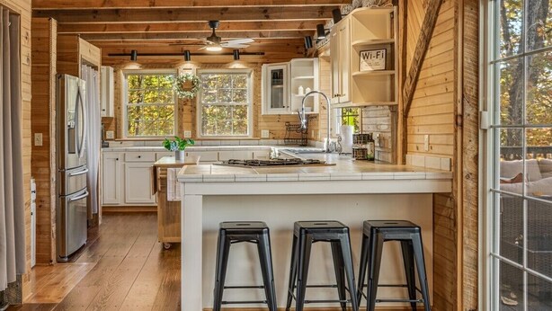 Une cuisine moderne avec des poutres en bois, un îlot central doté de tabourets et une grande fenêtre.